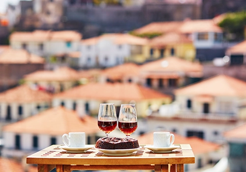 Two glasses of Madeira wine, two cups of fresh espresso coffee and traditional Portuguese honey and nut dessert bolo de mel in cafe with view to Funchal town, Madeira, Portugal
