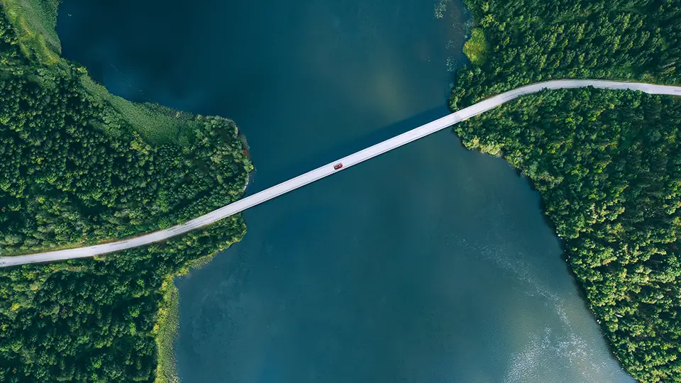 Aerial view of bridge road with red car over blue water lake or sea with island and green woods in summer Finland.